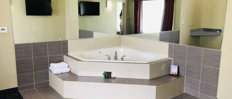 A modern bathroom with a freestanding bathtub, a large mirror, and a flat-screen TV mounted on the wall.