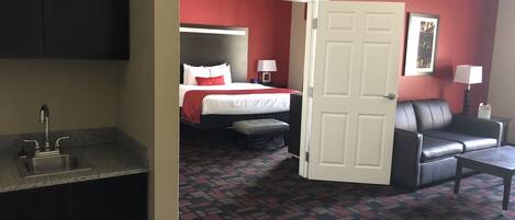 A hotel room with a bed, a desk, a chair, a sofa, a bathroom with a sink, and a patterned carpet.