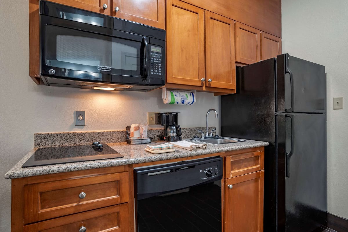 A kitchen with wooden cabinets, a black microwave, a black refrigerator, a granite countertop, a dishwasher, and a coffee maker.