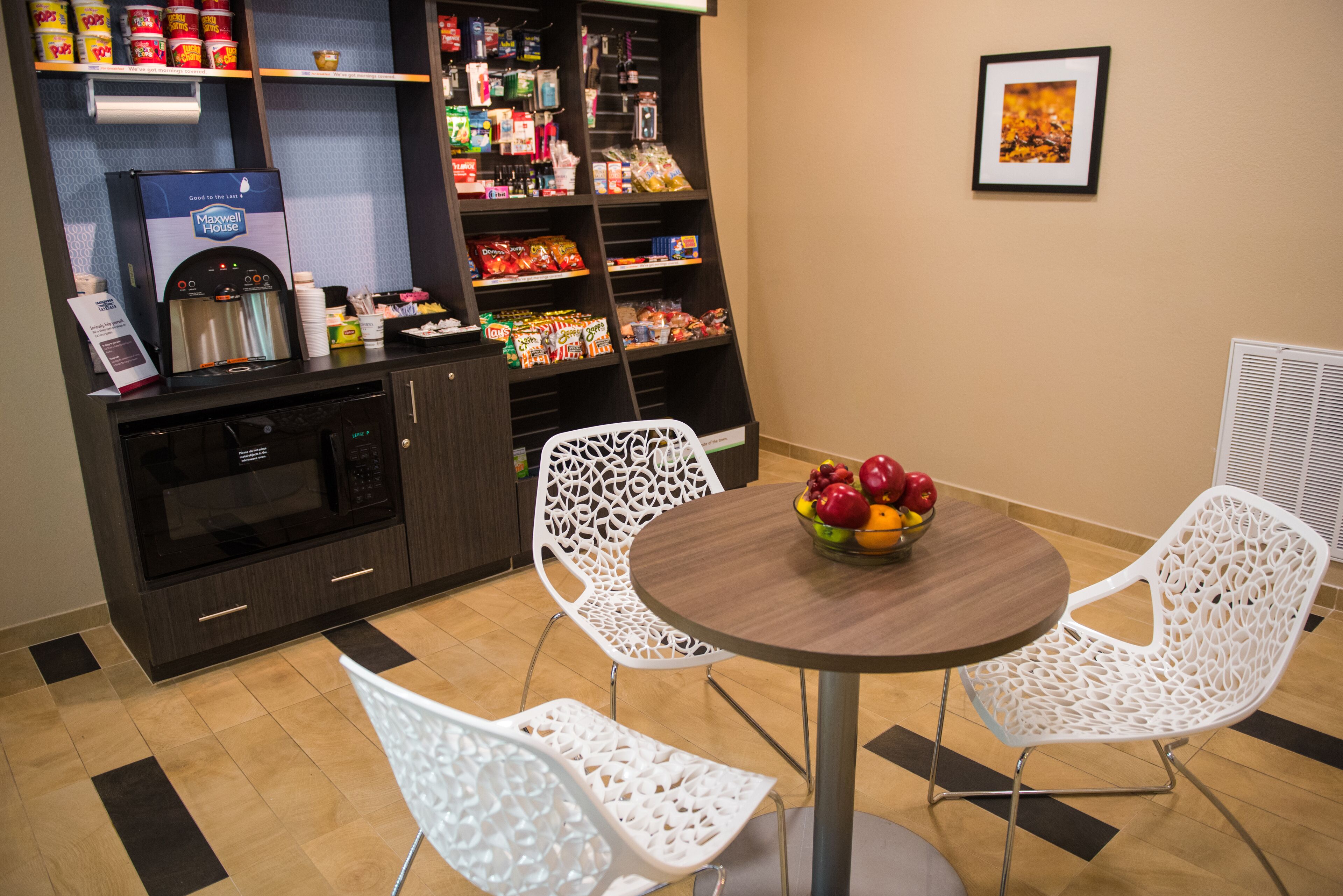 A dining area with a round table, white chairs, a microwave, a beverage dispenser, and a snack shelf.