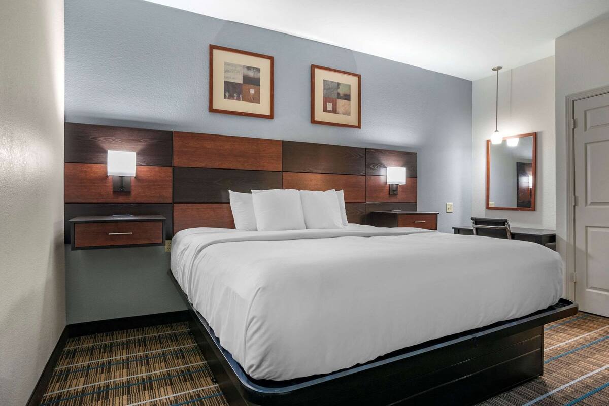 A hotel room with a large bed, two bedside tables, a nightstand, a desk, a chair, a mirror, and two framed pictures on the wall.
