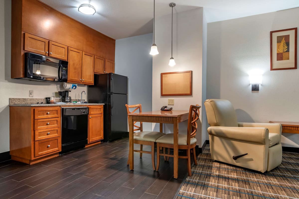 A compact kitchen with wooden cabinets, a microwave, a refrigerator, and a dishwasher. There is a dining table with chairs and a sofa.