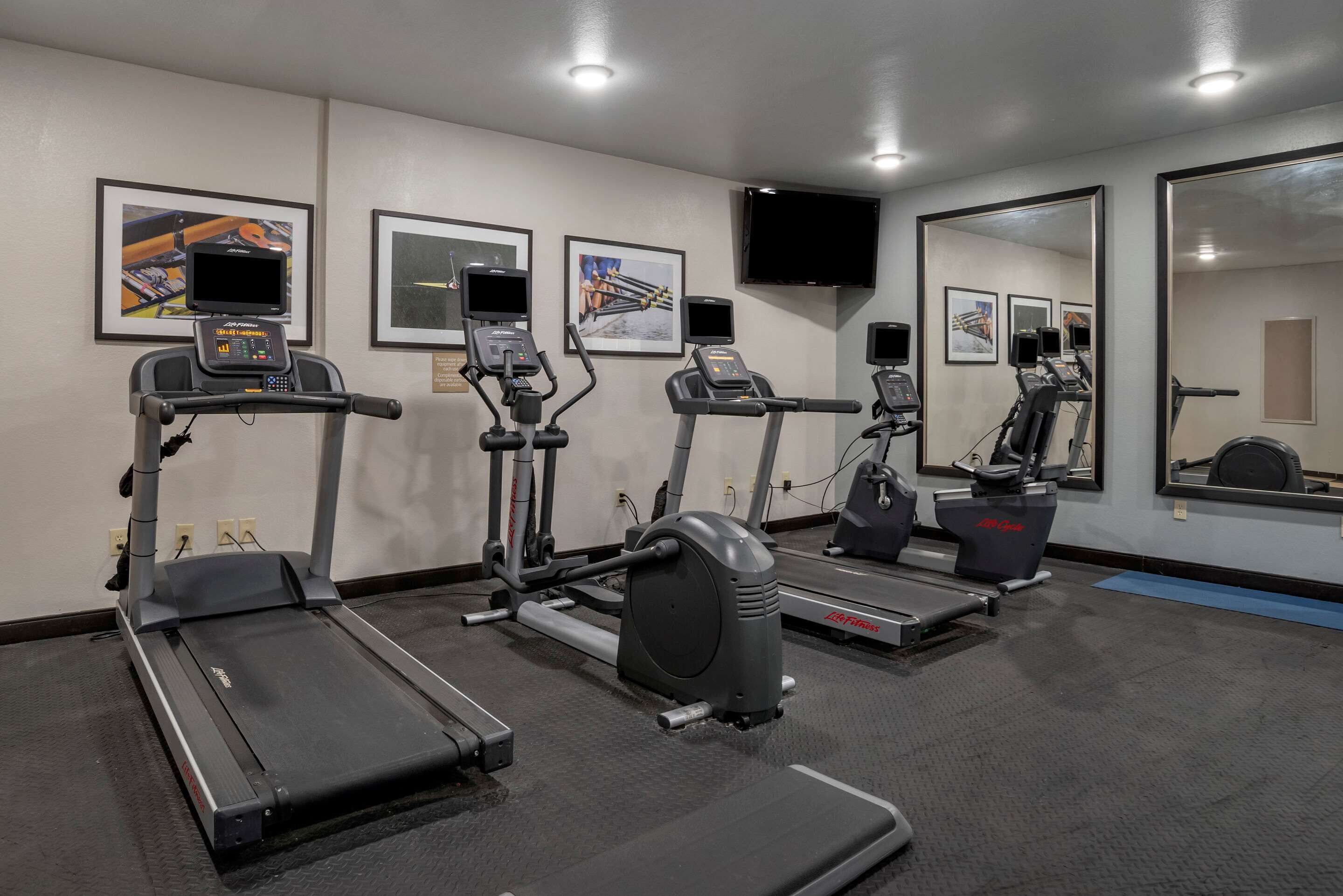 Un gimnasio con cintas de correr, elípticas y un espejo grande.