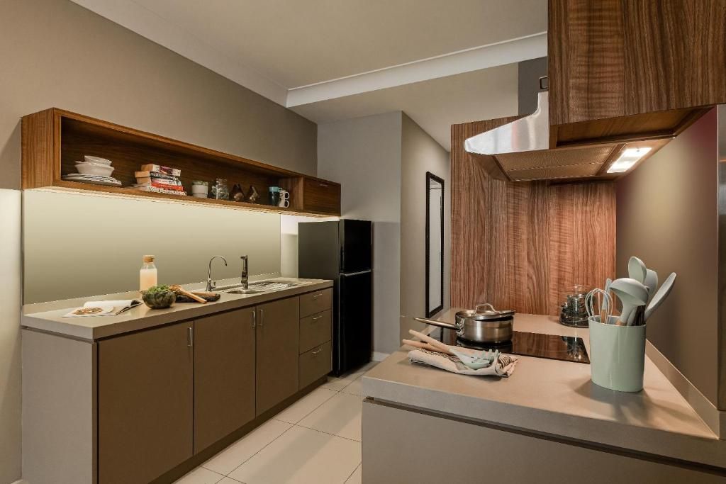 A modern kitchen with built-in wooden shelves, a stainless steel refrigerator, and a countertop with cooking utensils.