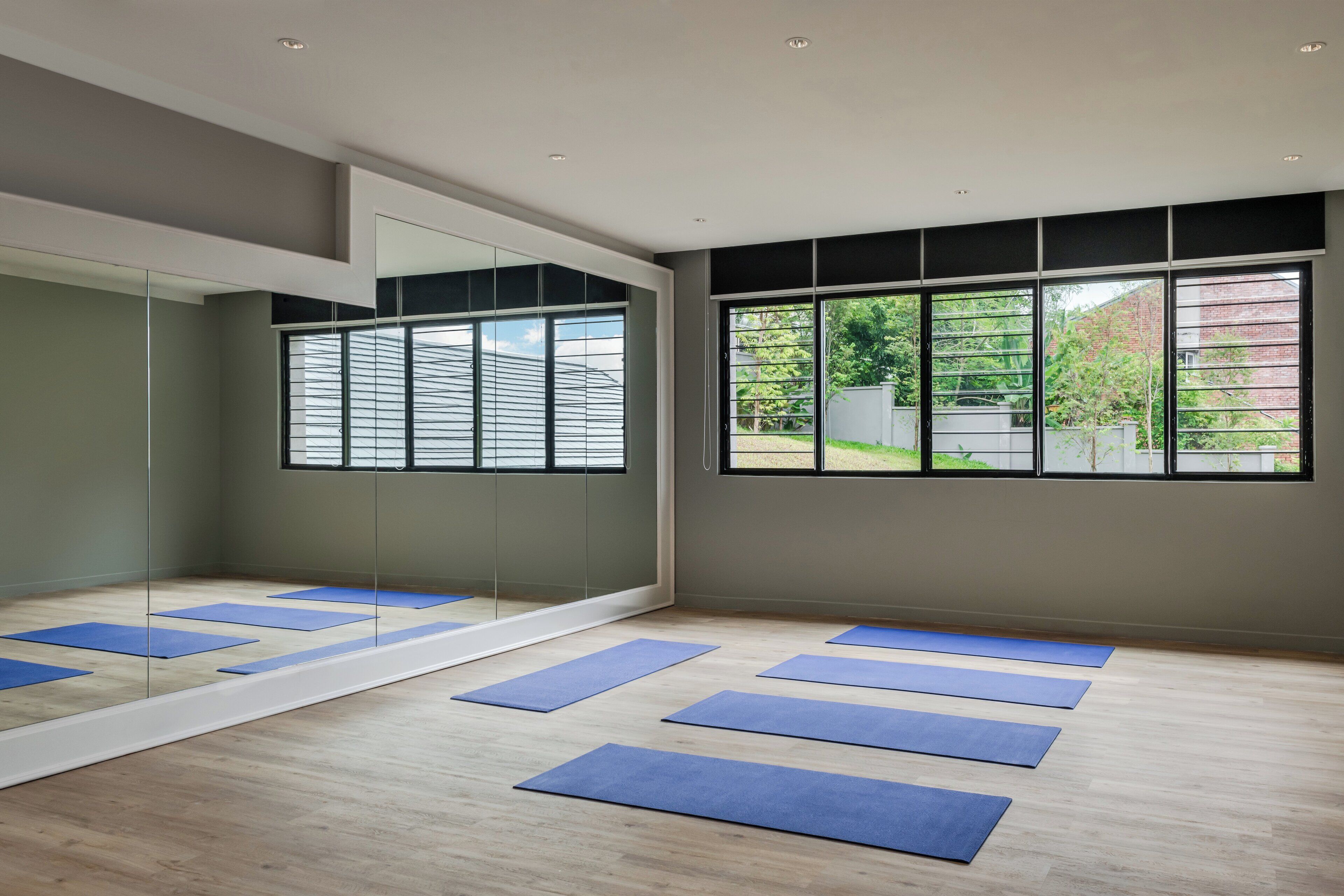 A yoga studio with mirrored walls, large windows, and blue mats on the floor.