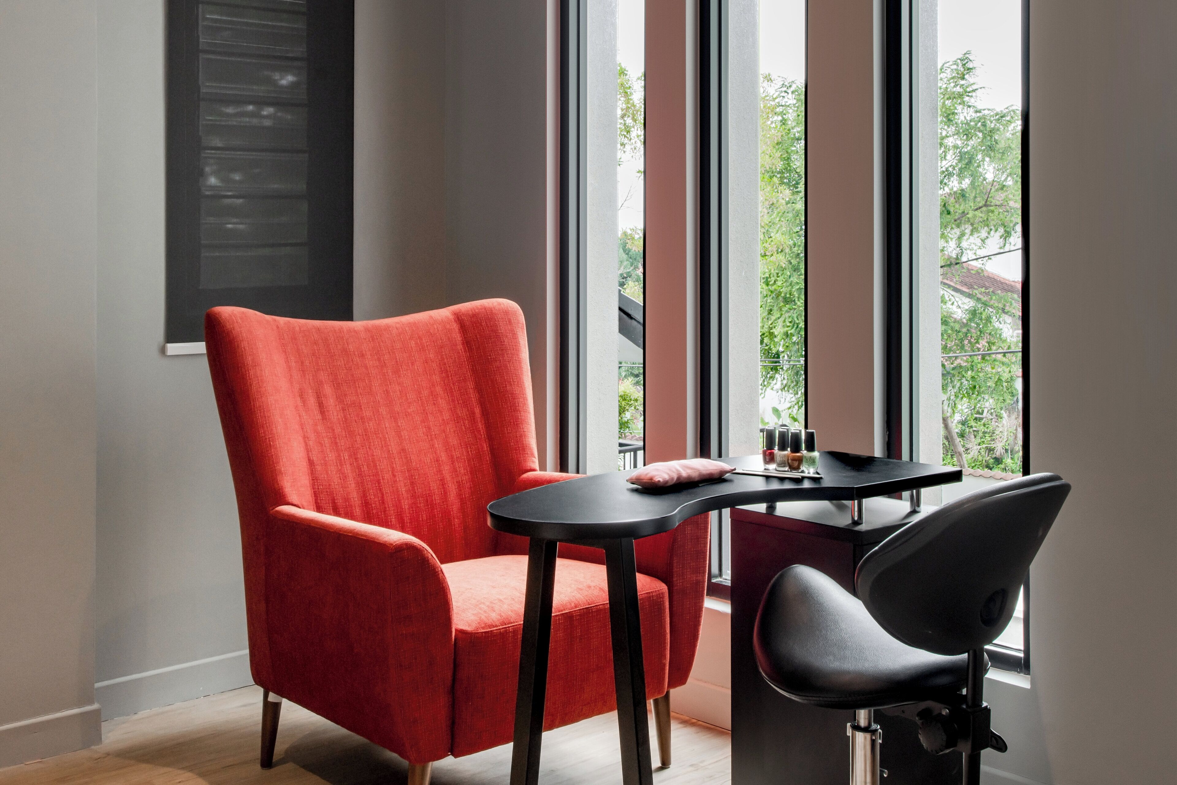 Una habitación moderna con un sillón rojo, una silla negra y una pequeña mesa con un cojín.