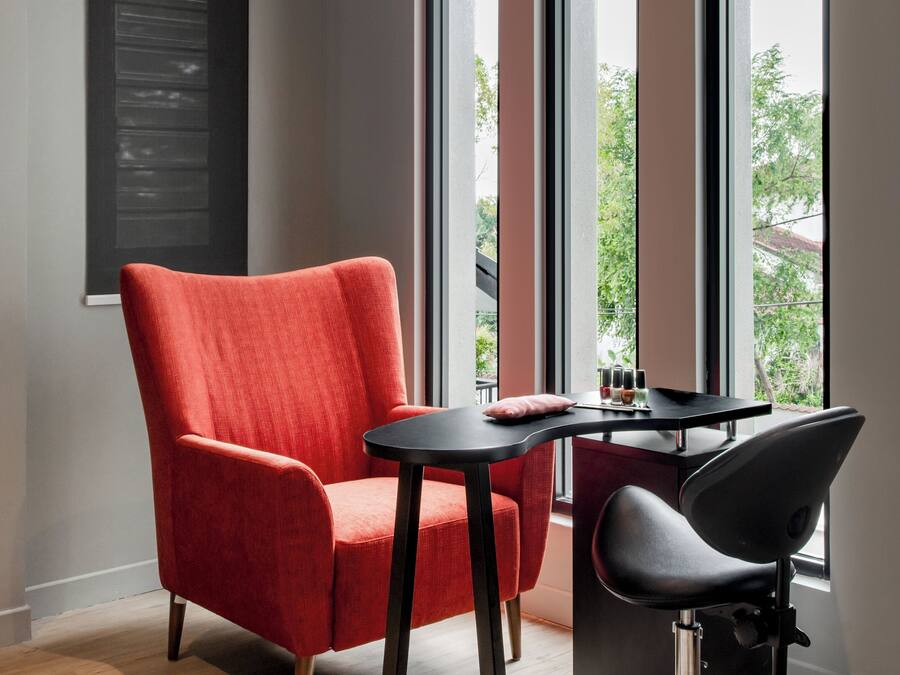 Una habitación moderna con un sillón rojo, una silla negra y una pequeña mesa con un cojín.