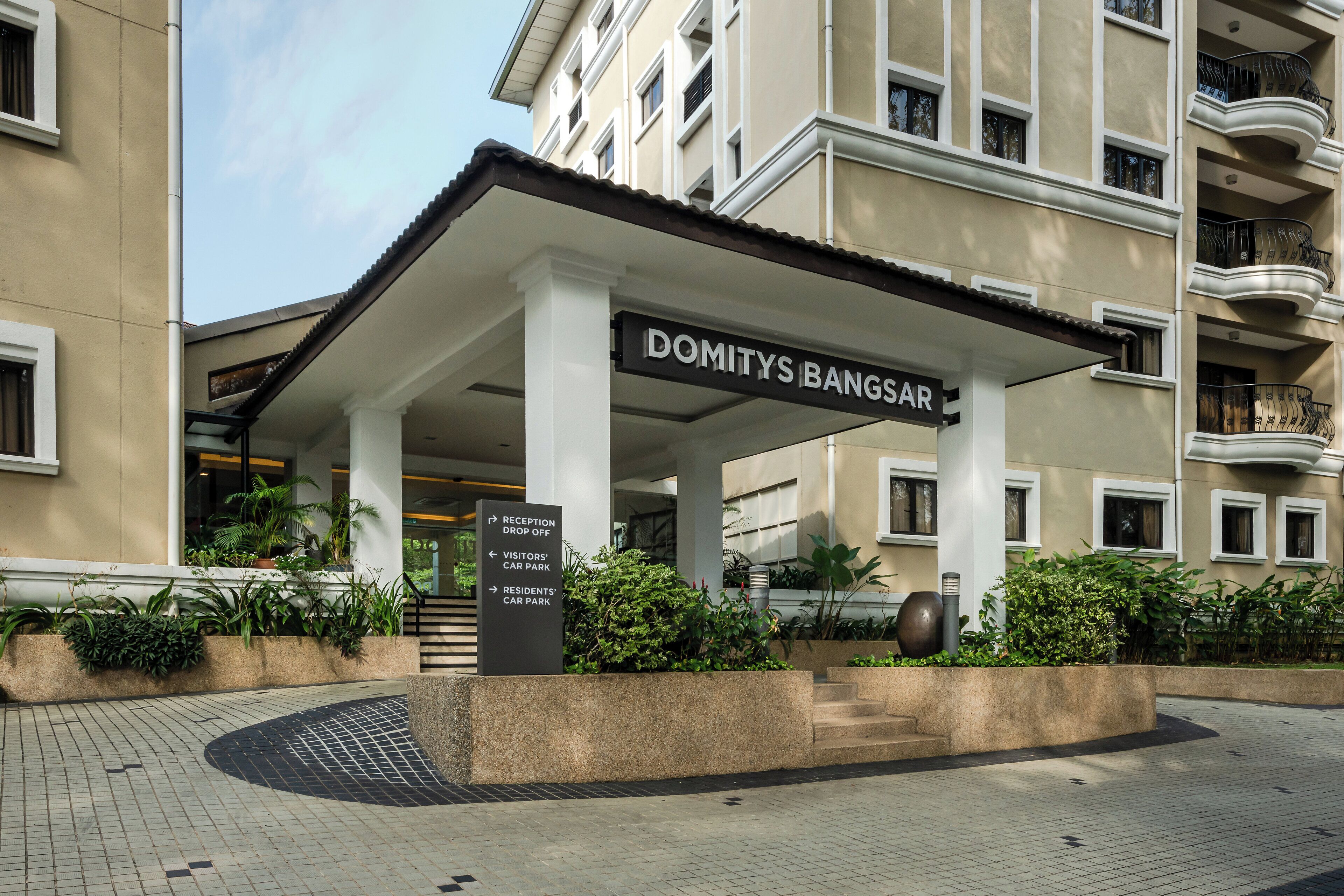 Ein Hotel Eingang mit einem Schild, auf dem ‚DOMITYS BANGSAR‘ steht, und Hinweisschildern für ‚RECEPTION SHOP OFF‘, ‚BESUCHER PARKPLATZ‘ und ‚ANWOHNER PARKPLATZ‘.