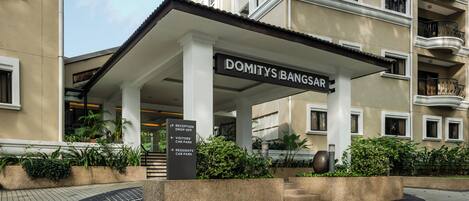 L’entrée d’un hôtel, avec une enseigne indiquant « DOMITYS BANGSAR » et des panneaux de signalisation indiquant « ACCÈS À LA RÉCEPTION ET AUX COMMERCES », « PARC AUTOMOBILE DES VISITEURS » et « PARC AUTOMOBILE DES RÉSIDENTS ».