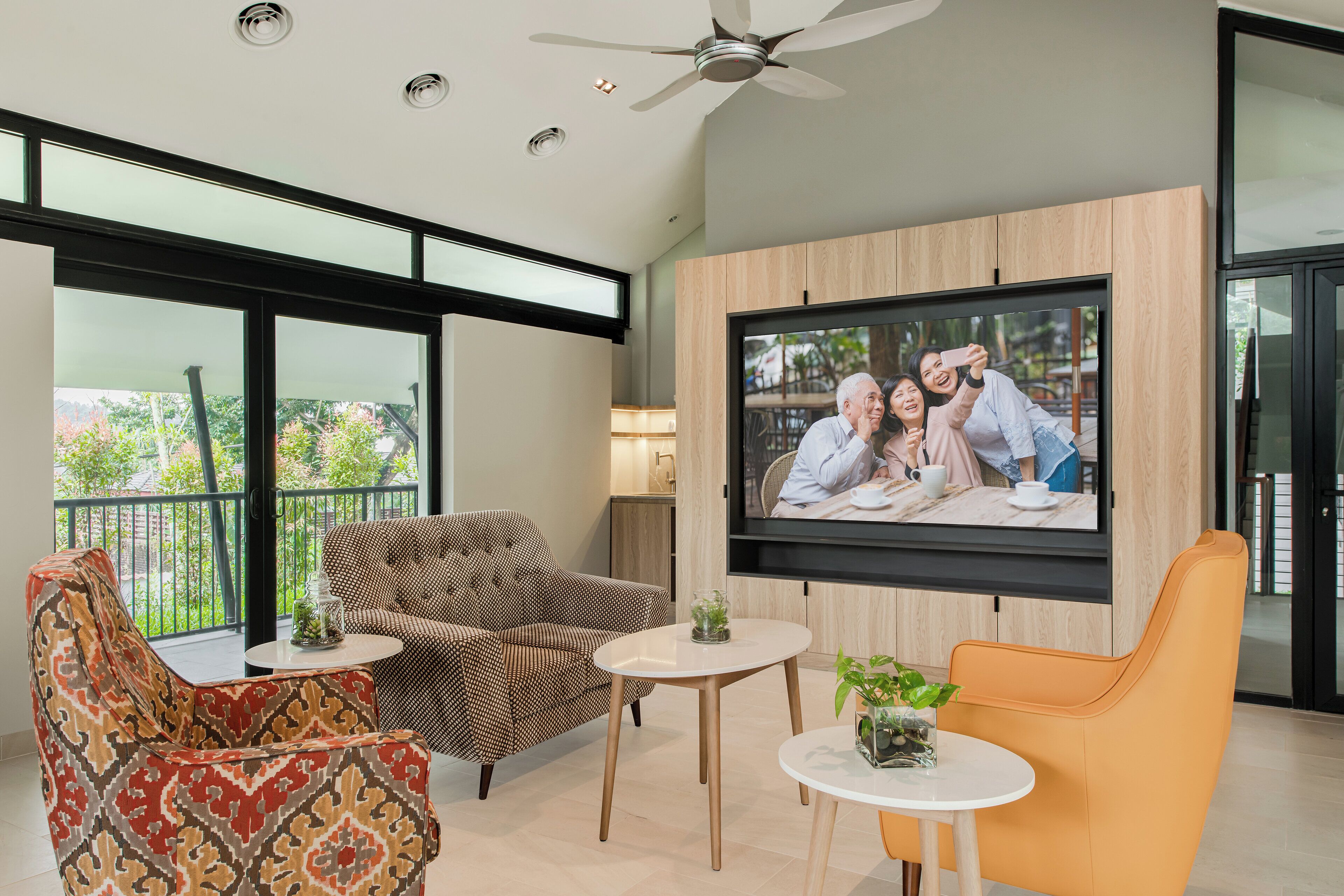 A modern living room with a large TV, comfortable seating, and a balcony view.