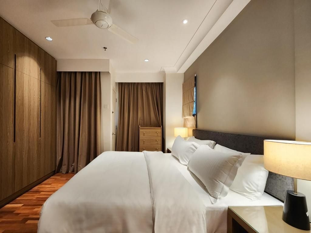 Une chambre d’hôtel avec un grand lit, une table de chevet, une lampe, une armoire et un ventilateur de plafond.