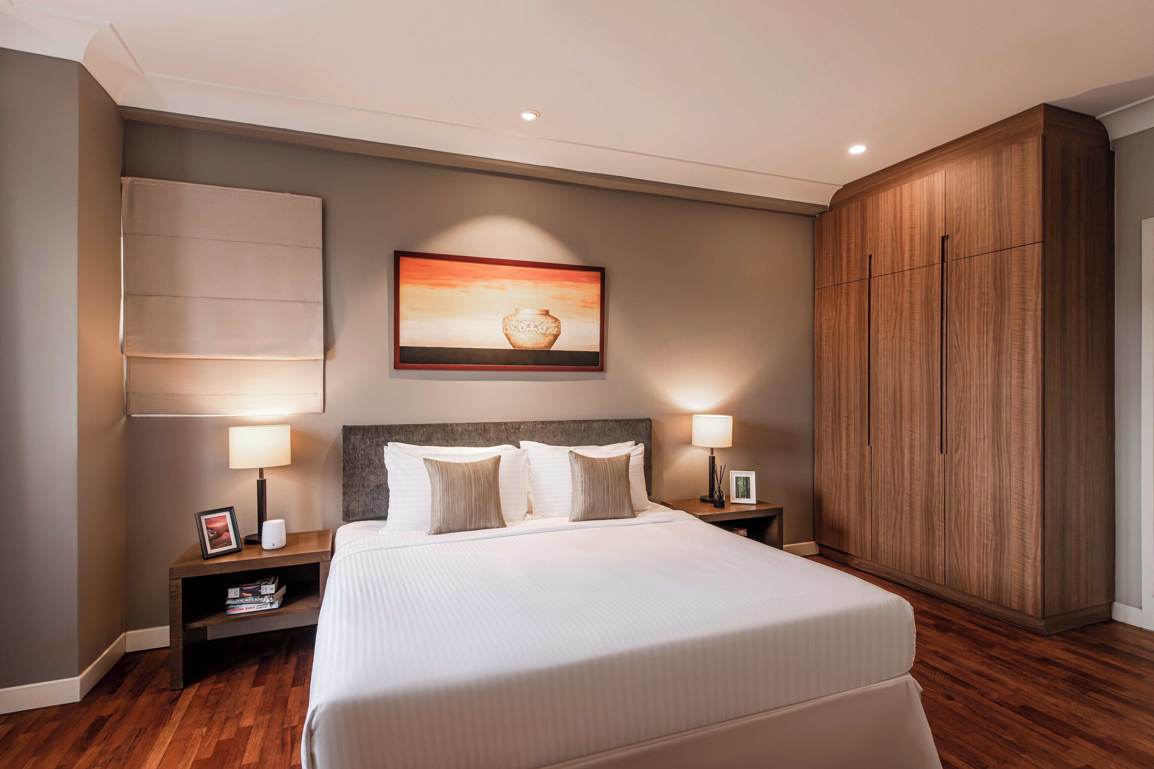 A hotel room with a large bed, two bedside tables with lamps, a wooden wardrobe, and a painting on the wall.