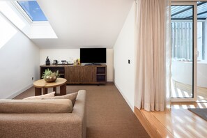 Una sala moderna con un sofá, una mesa de centro y un televisor sobre un mueble de madera. Hay un ventanal corredizo que da a un balcón.