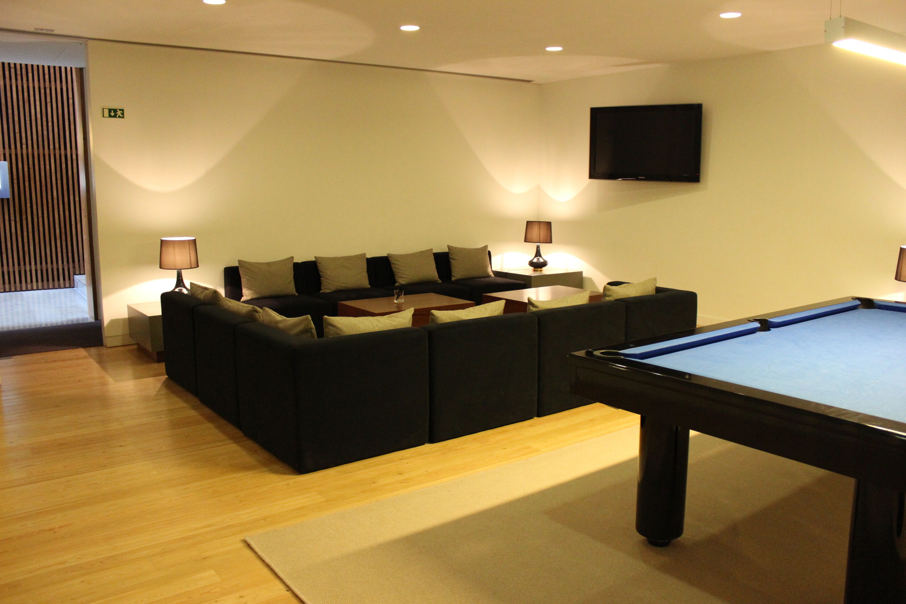 A room with a pool table, a sofa with cushions, two lamps, and a television on the wall.