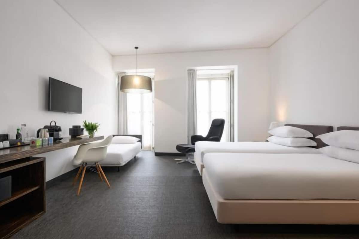 A hotel room with a bed, a desk, a chair, a TV, and a window.