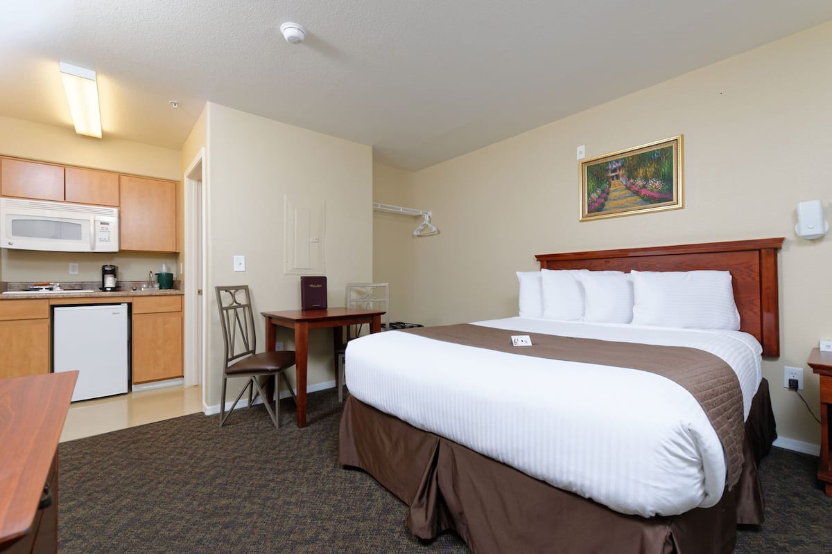 A hotel room with a bed, a desk, a microwave, and a small kitchenette.