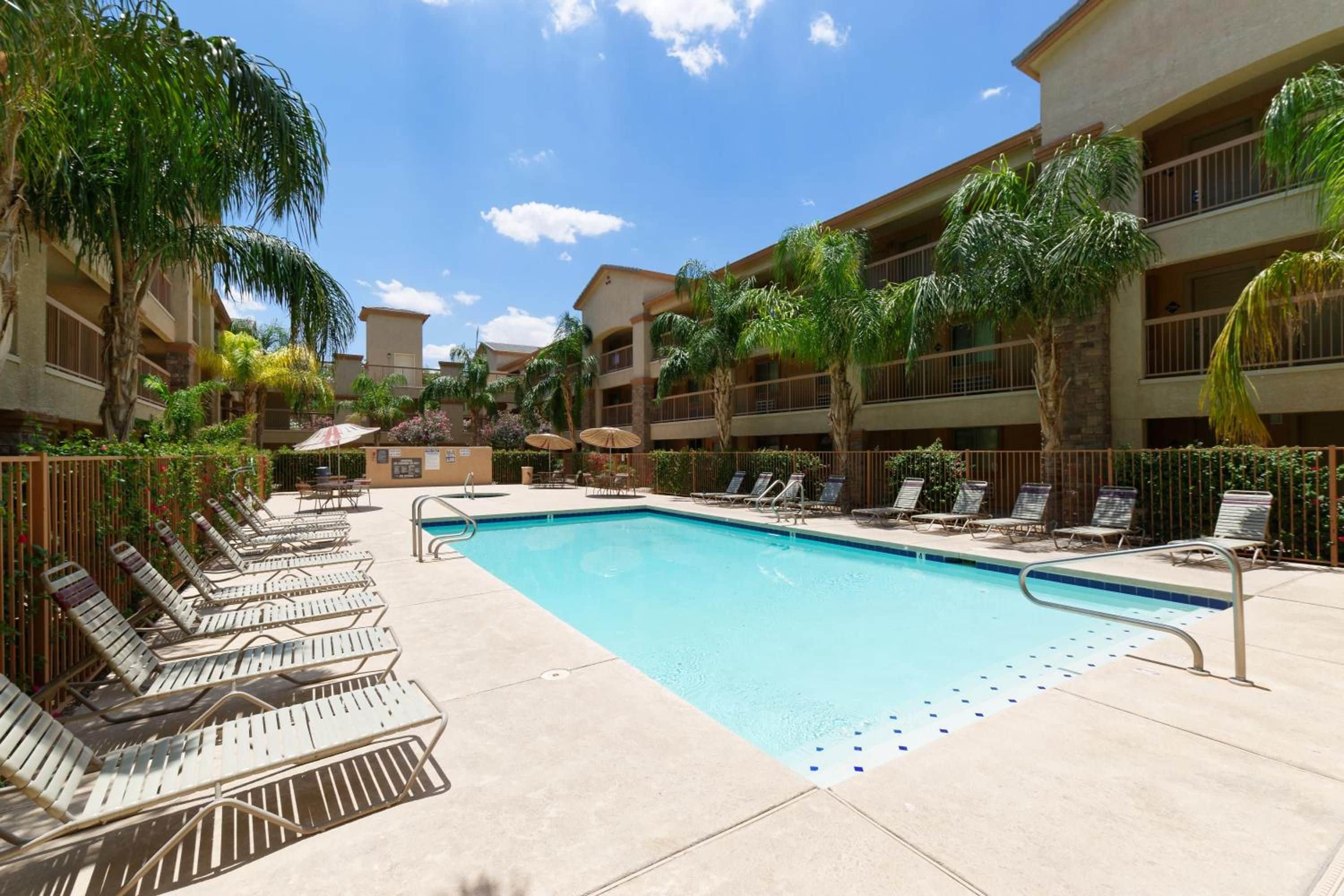 A hotel pool area with multiple lounge chairs and a clear blue pool.