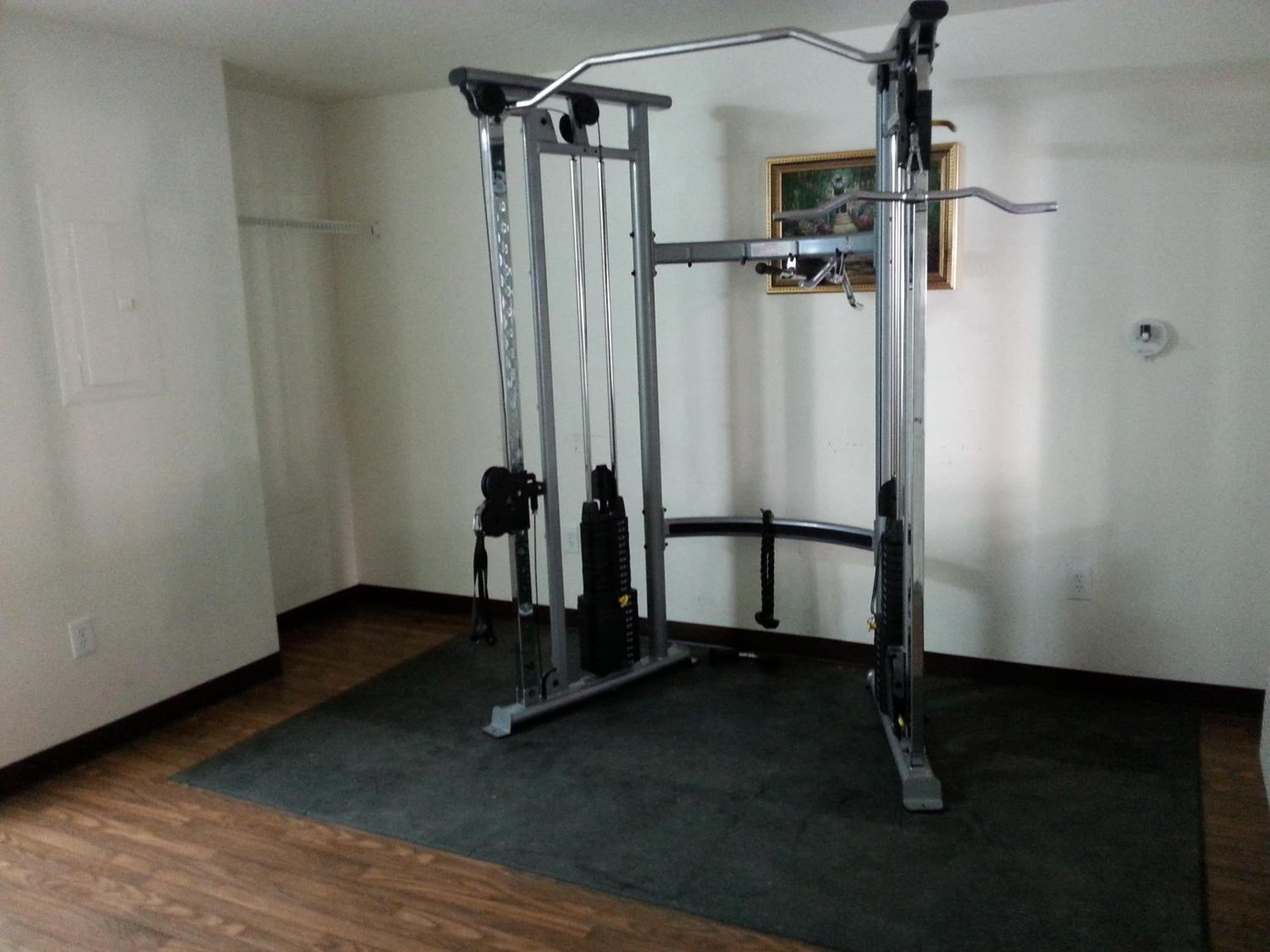 Una habitación con barra de dominadas y máquina de pesas frente a una pared blanca.