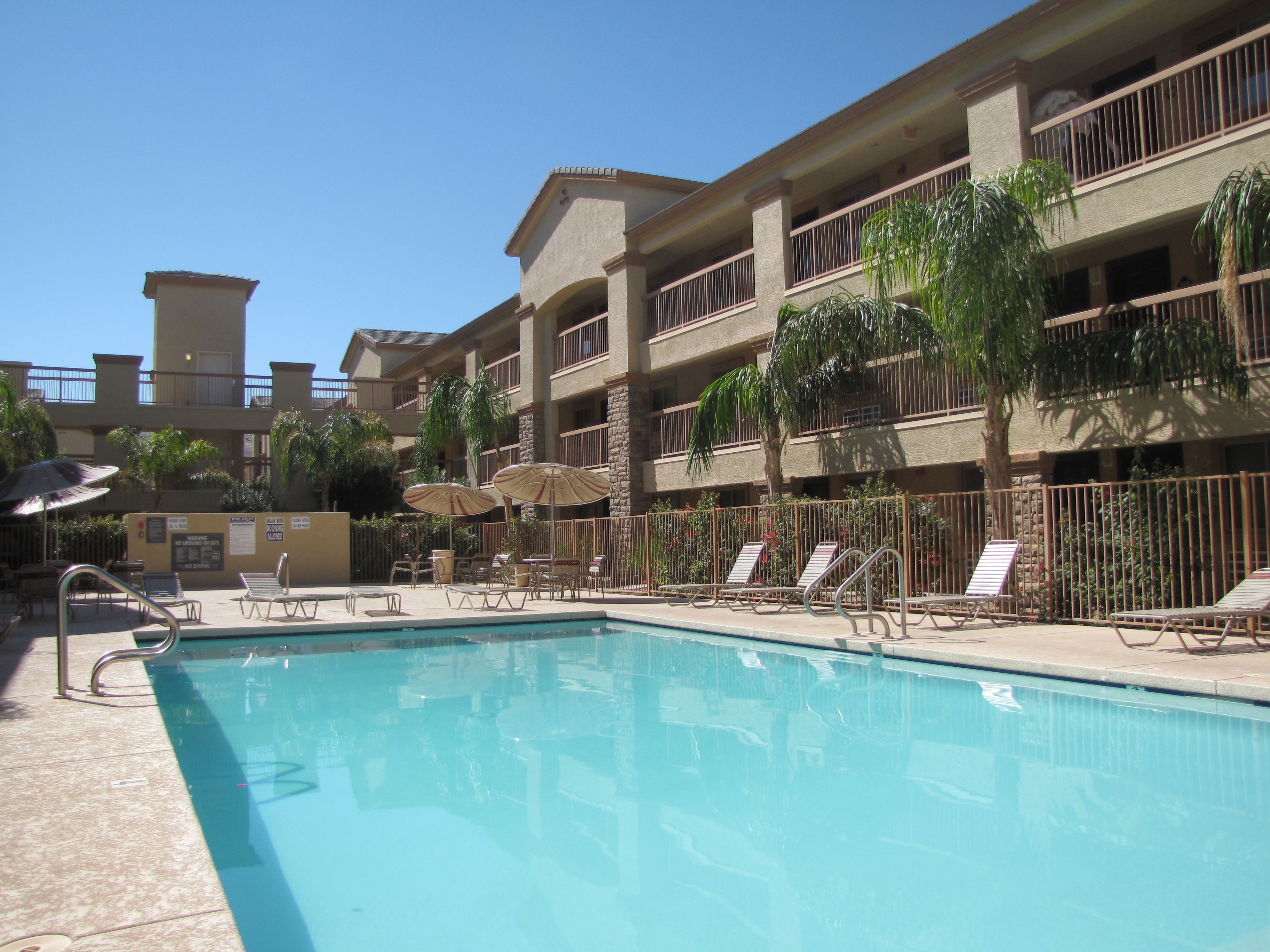 A pool area with lounge chairs and umbrellas, surrounded by a multi-story building with balconies.