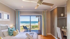 A bedroom with a large bed, a ceiling fan, a view of the ocean, and a balcony with a chair. - Boardwalk Lodge - self-catering (Wilderness)
