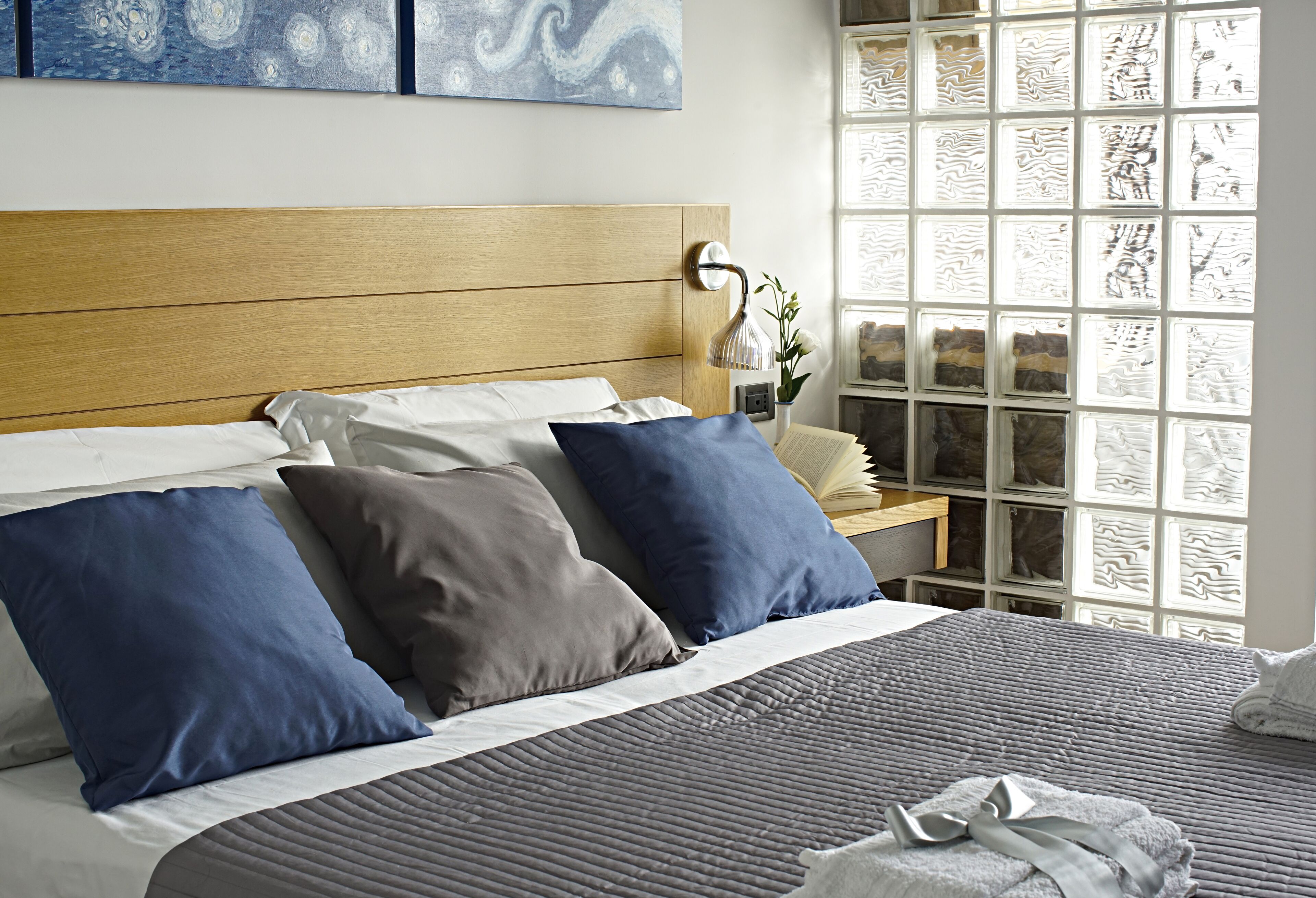 A neatly made bed with a wooden headboard, a bedside table with a lamp, and a window with patterned glass.