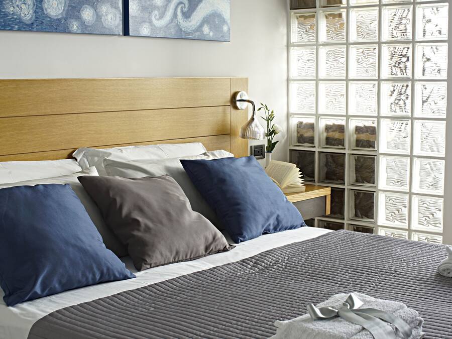A neatly made bed with a wooden headboard, a bedside table with a lamp, and a window with patterned glass.