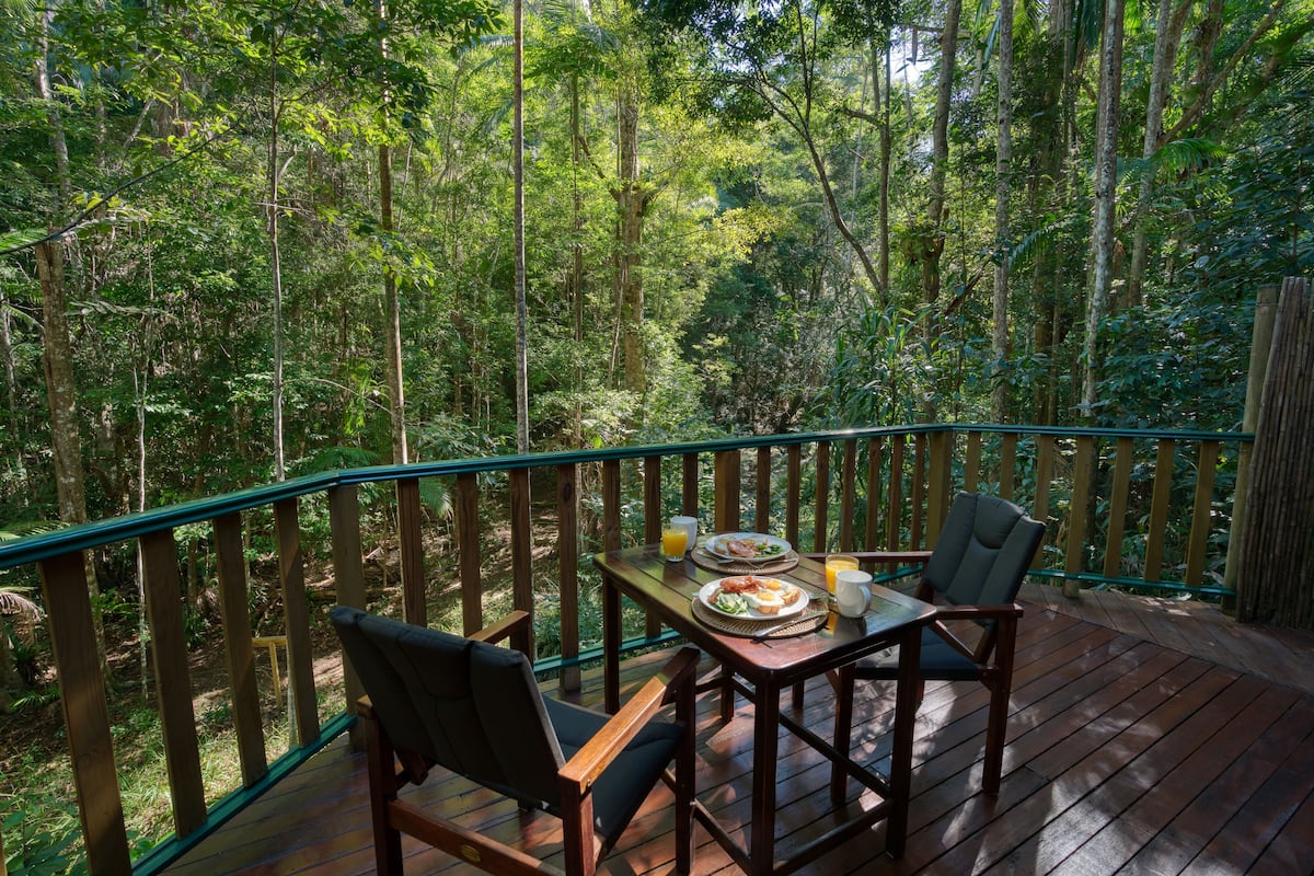 A wooden deck with a table and chairs overlooking a dense forest.