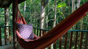 A hammock with a patterned cushion in a forested area with a wooden deck and railing.