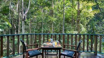 A wooden deck with a table set for breakfast, surrounded by chairs, overlooking a dense forest.