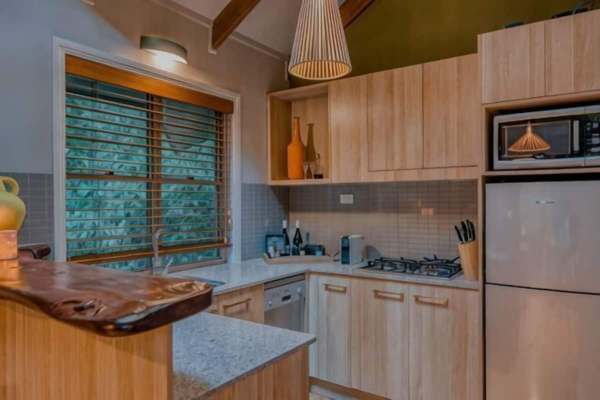A kitchen with wooden cabinets, a stainless steel refrigerator, and a window with blinds.