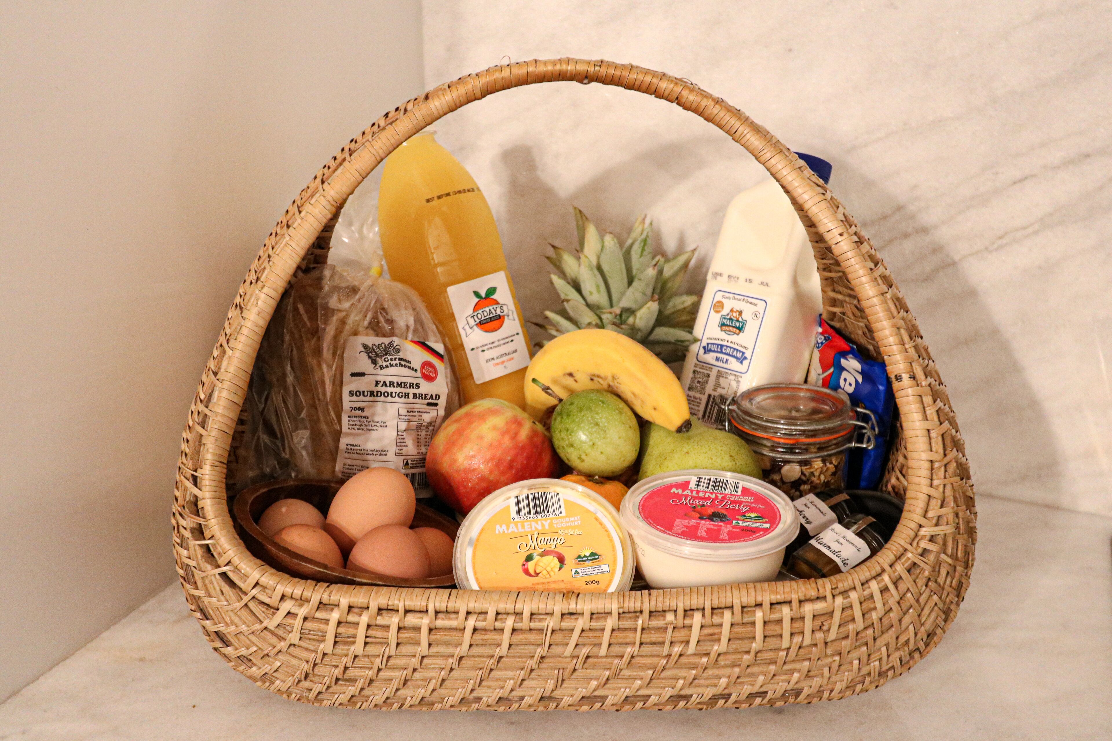A wicker basket containing various food items including eggs, fruits, a bottle of orange juice, and a jar of mixed berries.