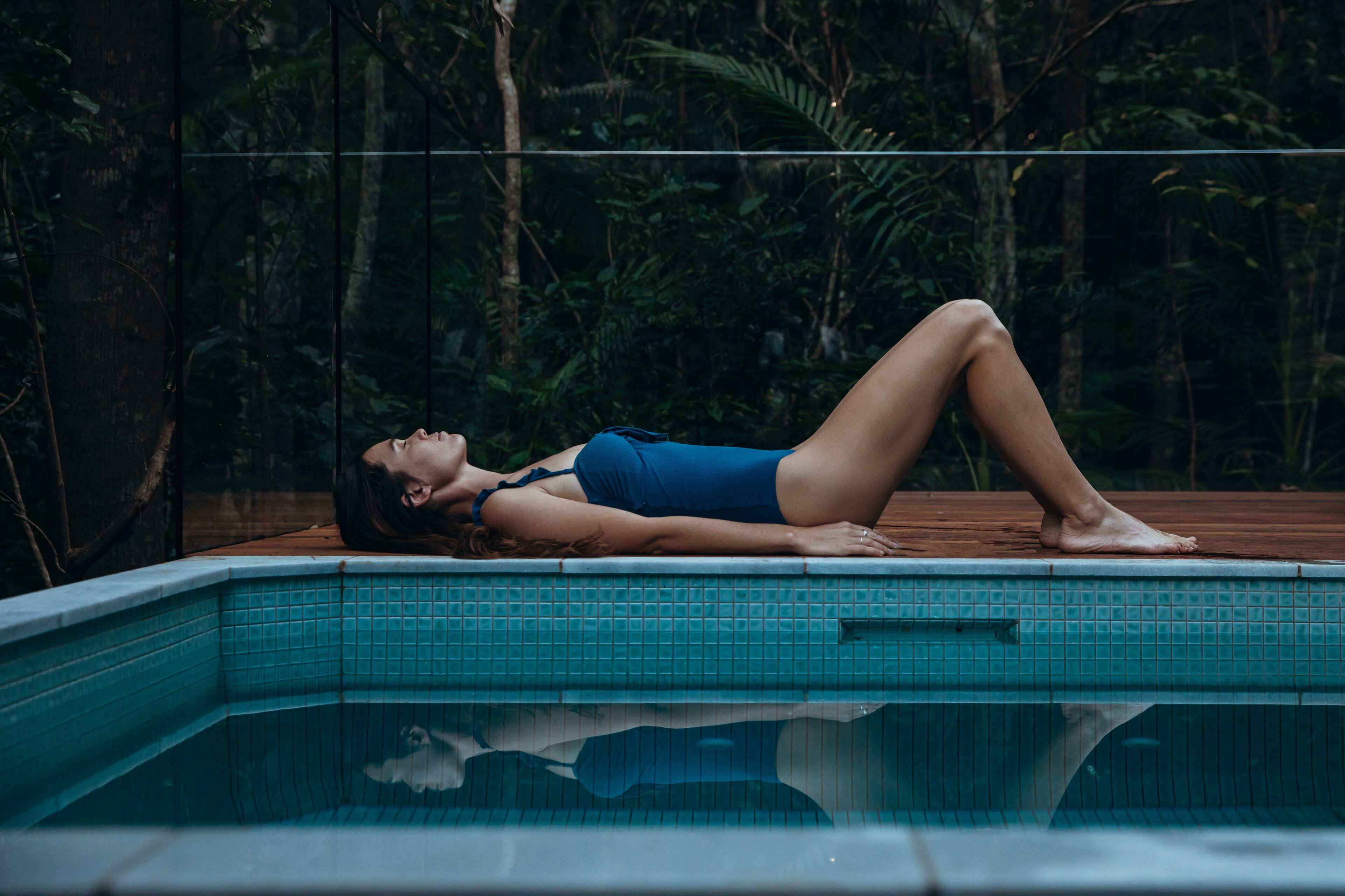 Una persona recostada en el borde de una piscina, con un bosque al fondo.