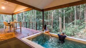 A hot tub with a wooden deck and a view of a forest.