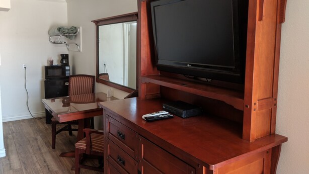 Una habitación con un mueble bajo de madera para el televisor, un televisor de pantalla plana, una mesita con una silla, un microondas y una cafetera.