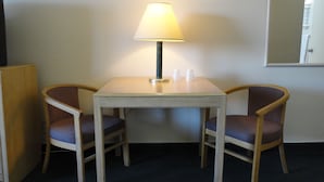 Una habitación pequeña con una mesa y dos sillas, una lámpara sobre la mesa y un espejo en la pared.
