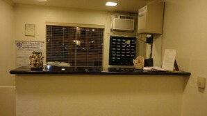 Un mostrador de recepción con una computadora, un tablón de anuncios y una ventana con persianas.