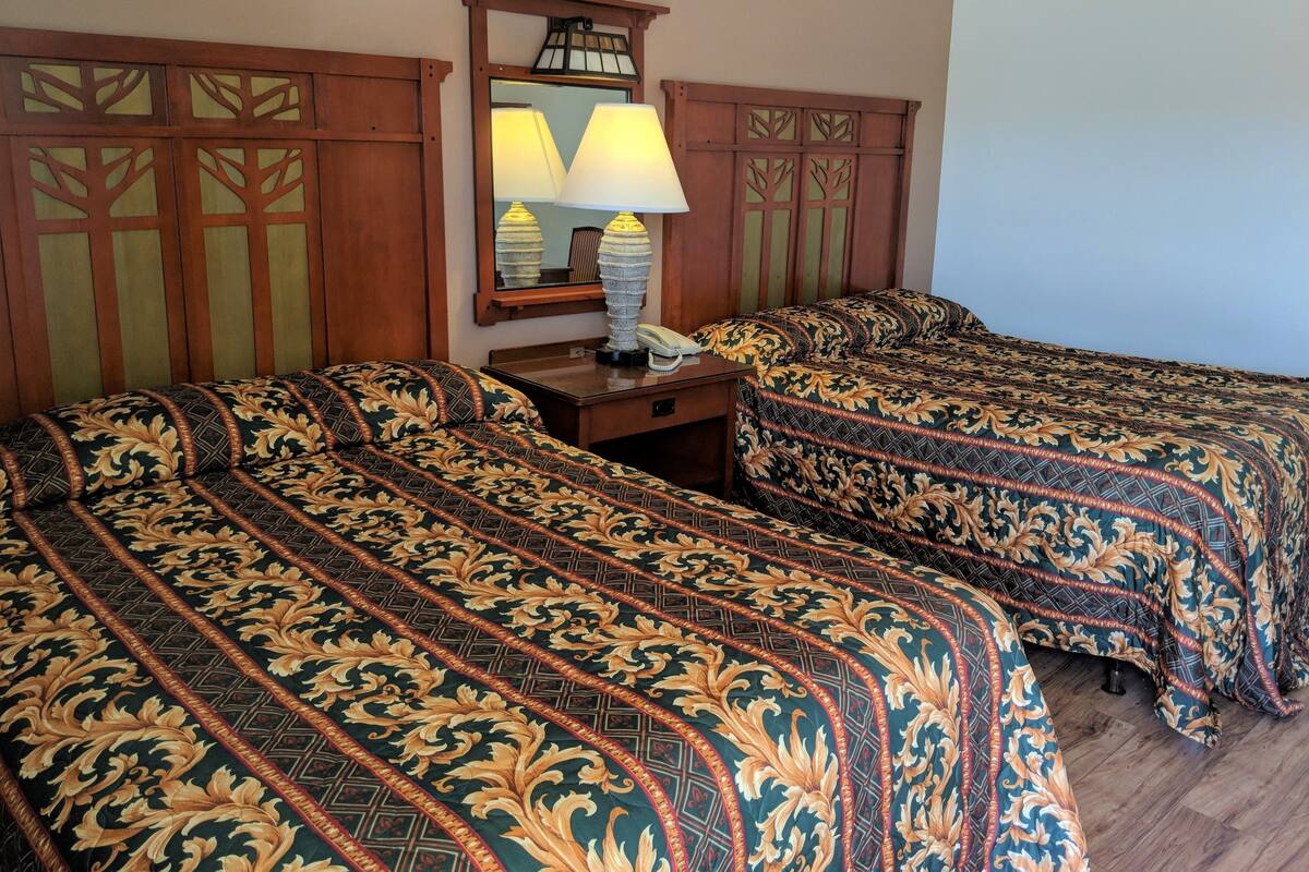 A hotel room with two beds, a nightstand, a lamp, and a mirror.