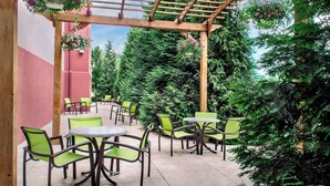 An outdoor patio with green chairs and tables, surrounded by lush greenery and a wooden pergola. - SpringHill Suites by Marriott Long Island Brookhaven (Yaphank)