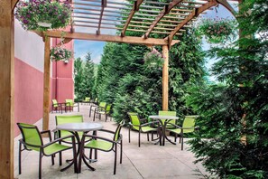 An outdoor patio with green chairs and tables, surrounded by lush greenery and a wooden pergola. - SpringHill Suites by Marriott Long Island Brookhaven (Yaphank)