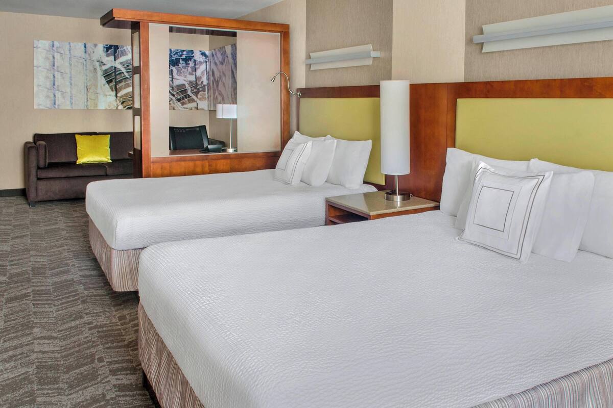 Habitación de hotel con dos camas, un sofá, un escritorio y un espejo.