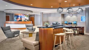 A modern hotel lobby with a reception desk, seating area, and bar. - SpringHill Suites by Marriott Long Island Brookhaven (Yaphank)
