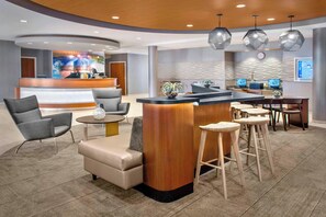 A modern hotel lobby with a reception desk, seating area, and bar. - SpringHill Suites by Marriott Long Island Brookhaven (Yaphank)