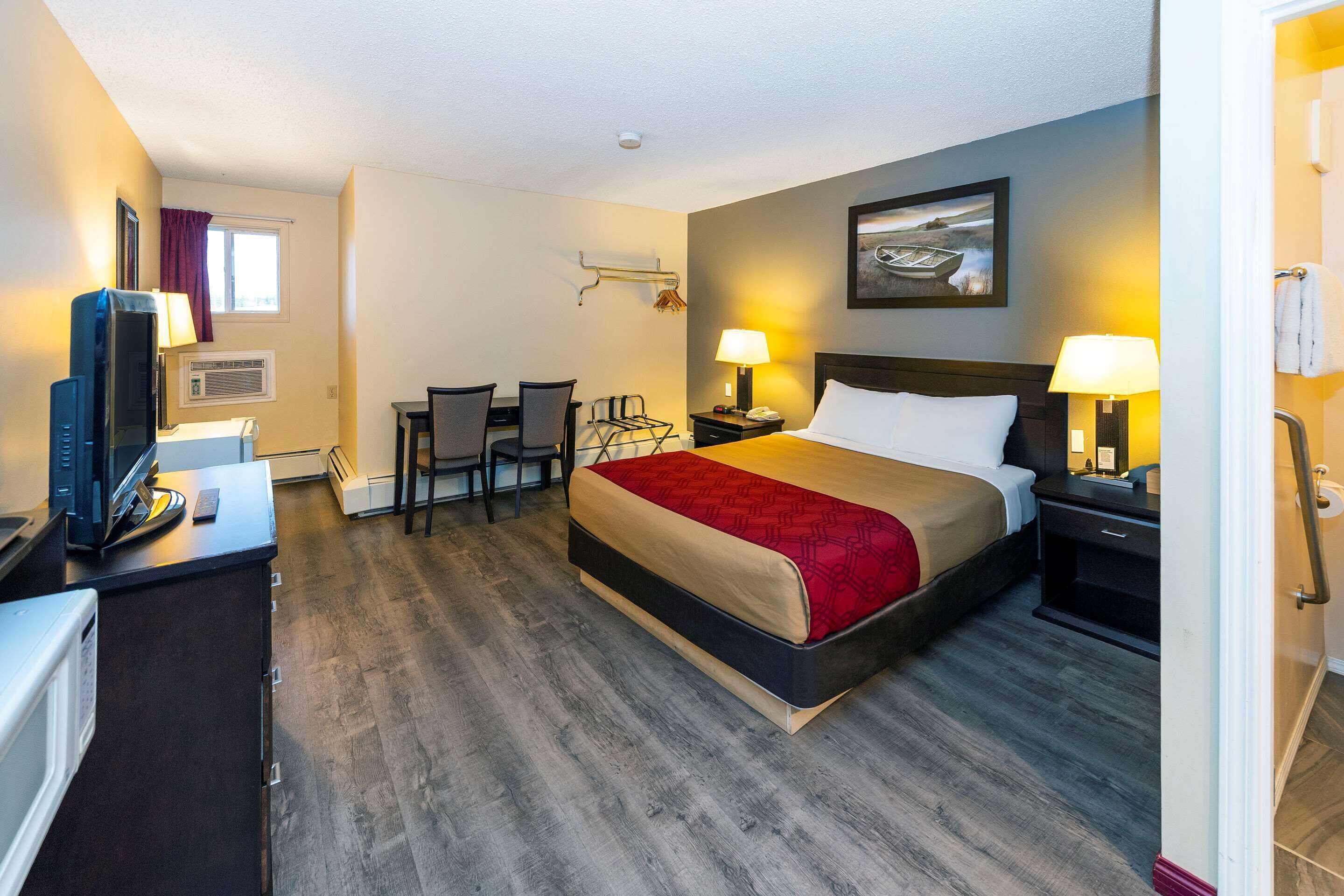 A hotel room with a bed, desk, chairs, and a television.