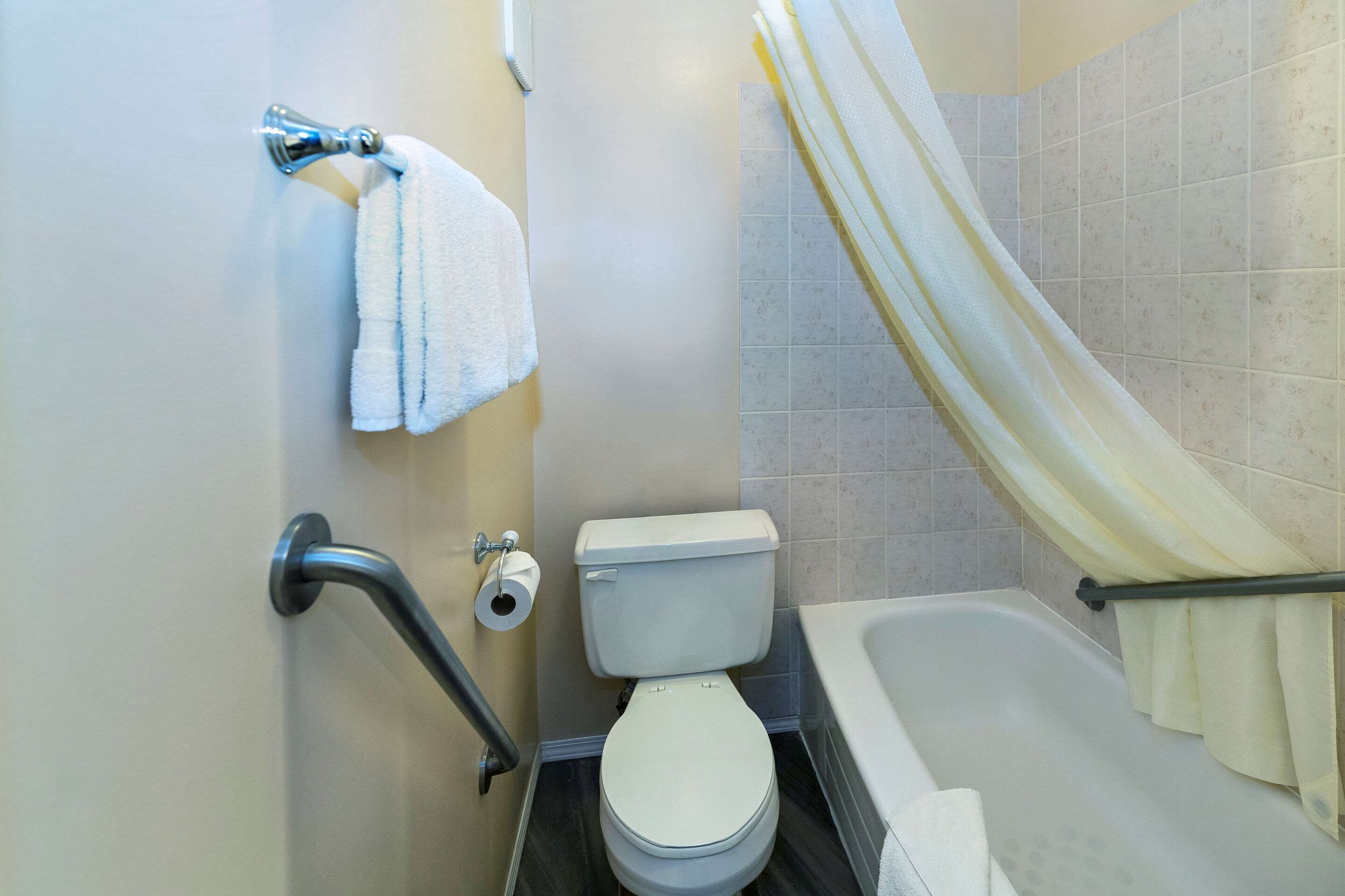 Un baño con inodoro, bañera, cortina de ducha y barandilla.