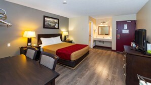 A hotel room with a bed, bedside tables, a desk, chairs, a TV, a mirror, and a bathroom with a sink and mirror. - Econo Lodge Edson - 2nd Ave (Edson)