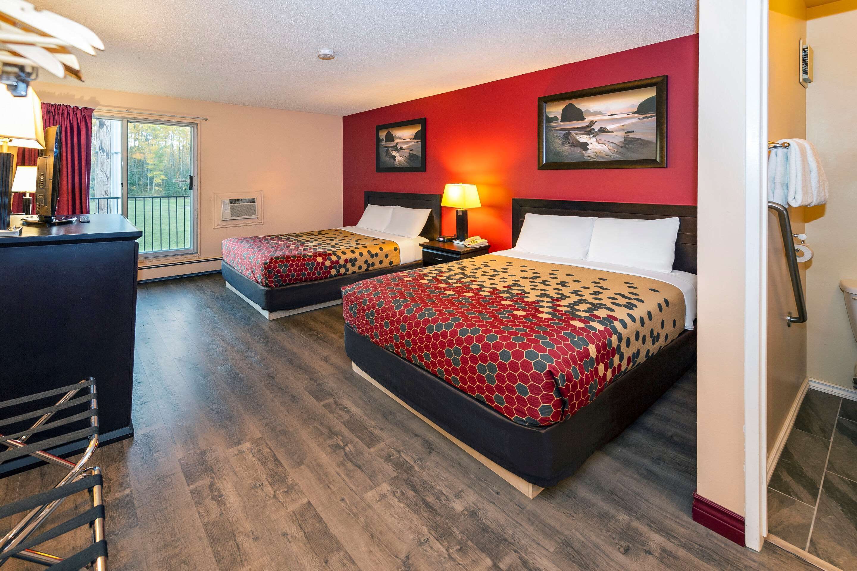 A hotel room with two beds, a desk, and a view of the outdoors.