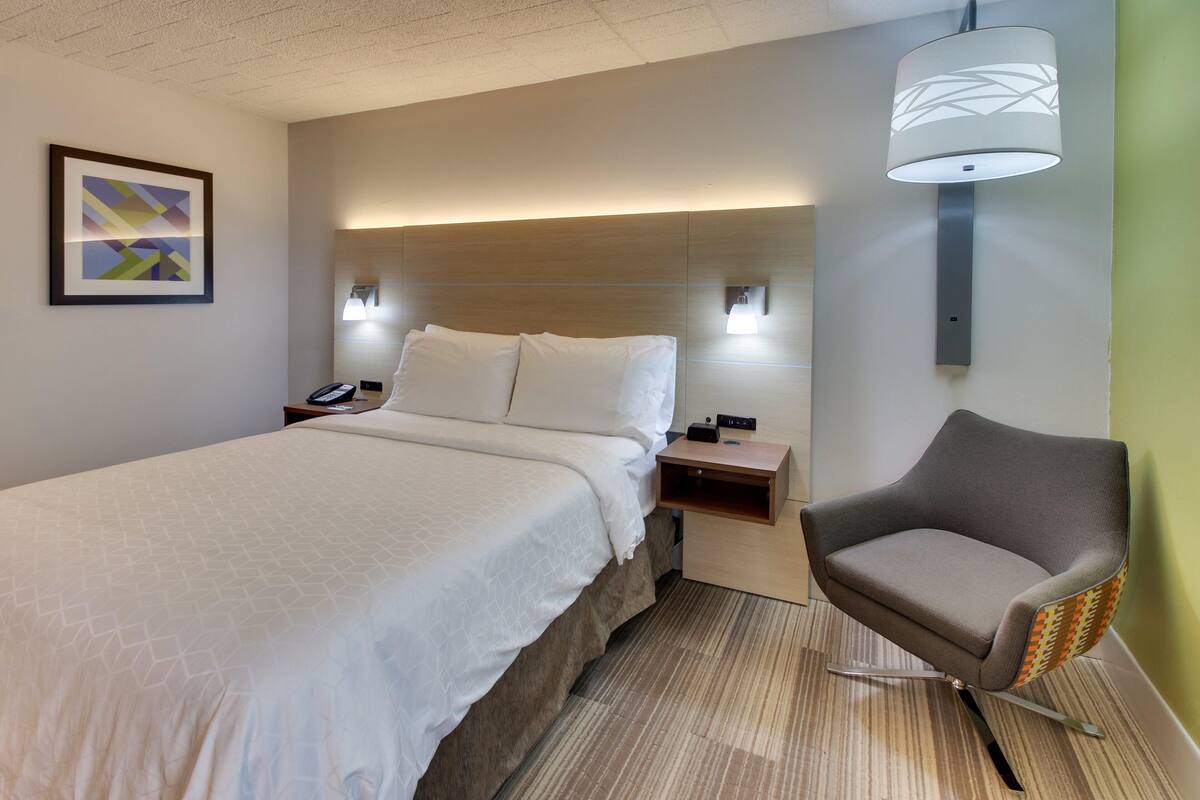 Habitación de hotel con cama, mesitas de noche, una silla y una lámpara fijada a la pared.