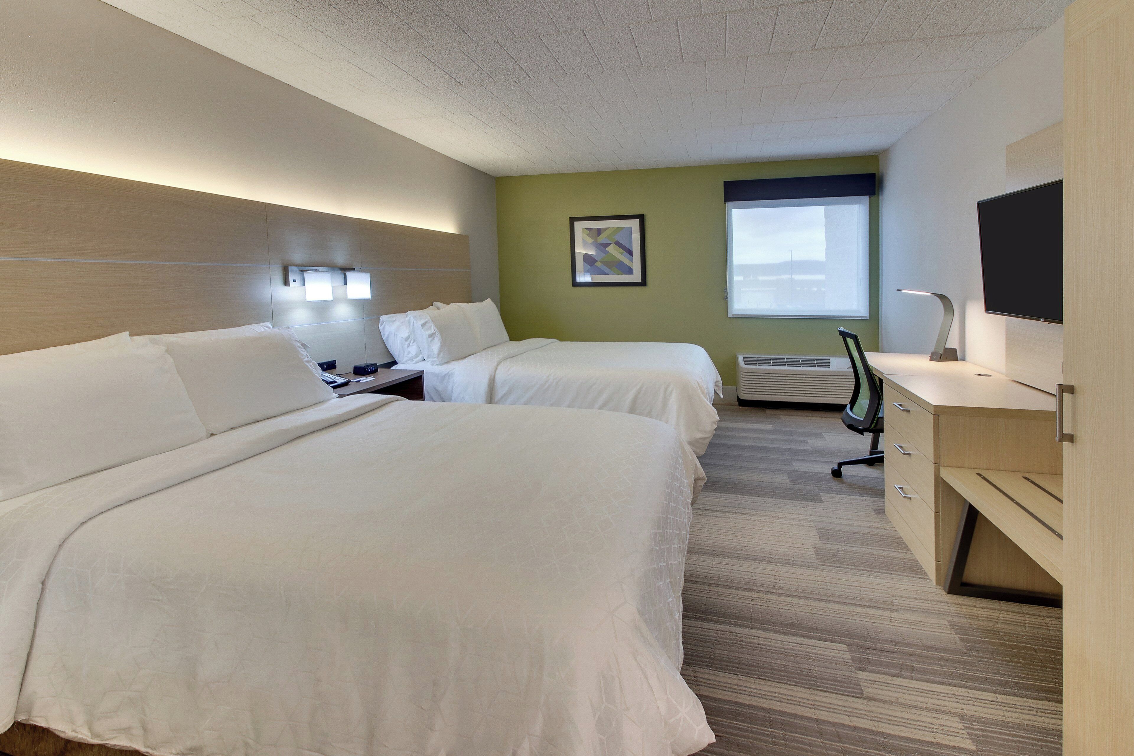 Ett hotellrum med två sängar, ett skrivbord, en stol, en platt-TV och ett fönster.