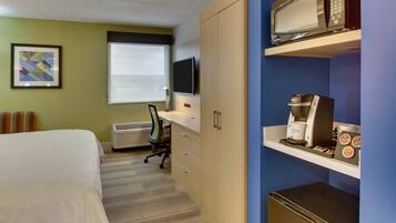 Ein Hotelzimmer mit Bett, Schreibtisch, Computer, Klimaanlage, Kaffeemaschine und Mikrowelle.
