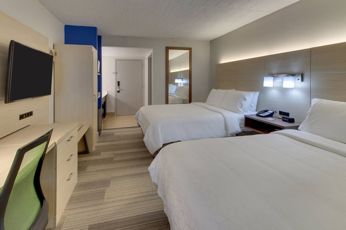 Une chambre d’hôtel avec deux lits, un bureau avec une chaise, une télévision et un miroir.
